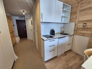A compact kitchen with white cabinets, a built-in dishwasher, and a wooden wall. - Studio cabin near slopes - 4 guests (Tignes)