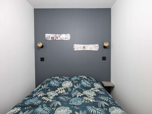A bedroom with a bed, two wall-mounted decorative items, and a small wooden nightstand. - Modern apartment with parking - 4 guests (Saint-Lary-Soulan)
