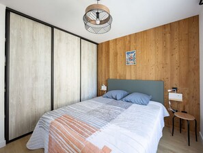A bedroom with a bed, a nightstand, a wall-mounted light, and a wooden panel wall. - Modern apartment with parking - 4 guests (Saint-Lary-Soulan)