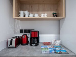 A kitchen area with a wooden shelf holding white cups, a red coffee maker, a toaster, and a coffee pod box. - Modern apartment with parking - 4 guests (Saint-Lary-Soulan)