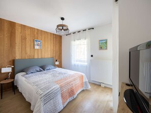 Een slaapkamer met een bed, nachtkastjes, een televisie, houten wanden, een raam met gordijnen en een radiator.