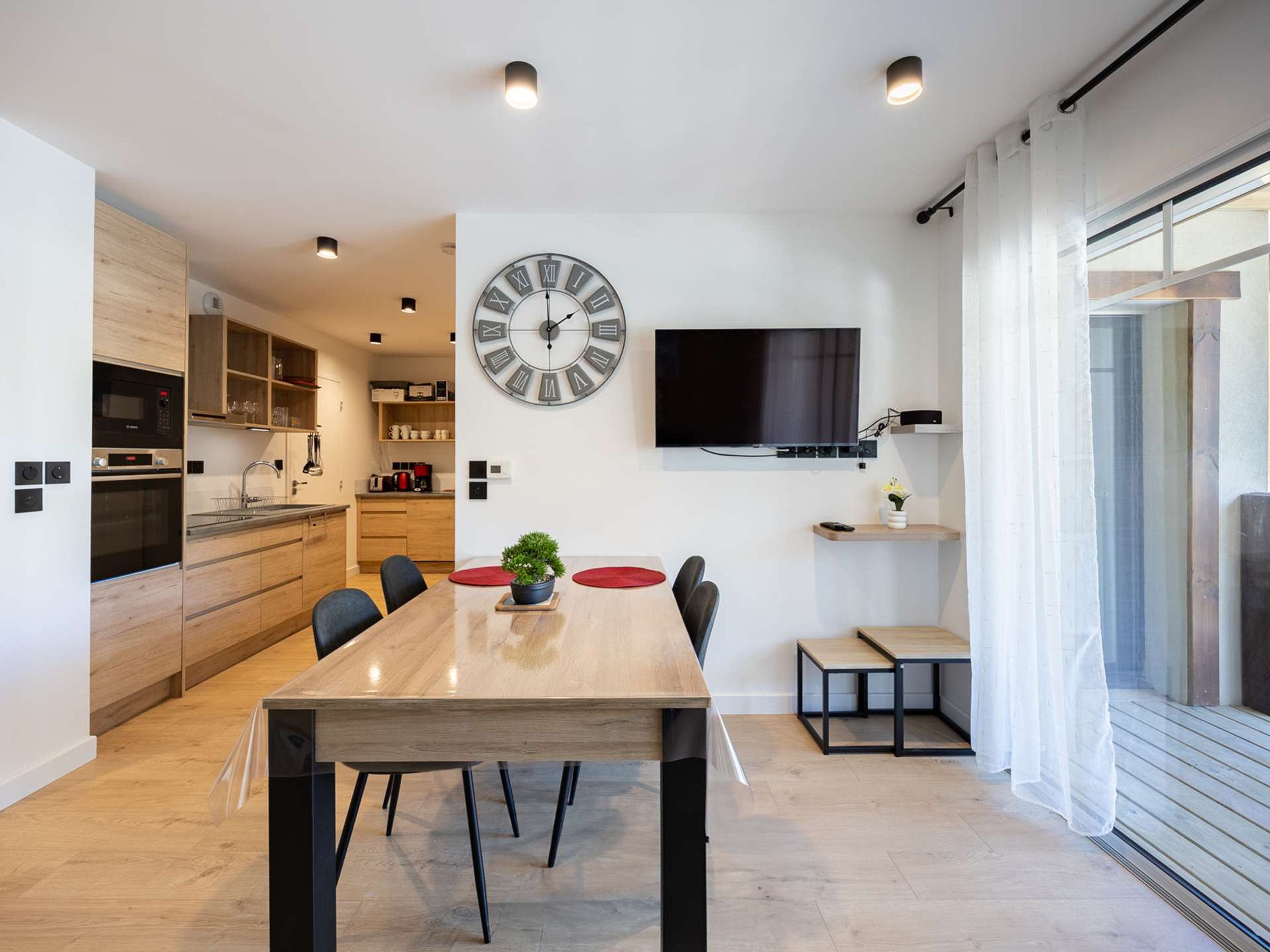 A modern kitchen with built-in appliances, a dining area with a large wooden table, and a wall-mounted TV.