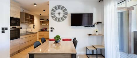 A modern kitchen with built-in appliances, a dining area with a large wooden table, and a wall-mounted TV.