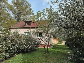 A two-story building with a red roof, surrounded by lush greenery and flowering trees.
