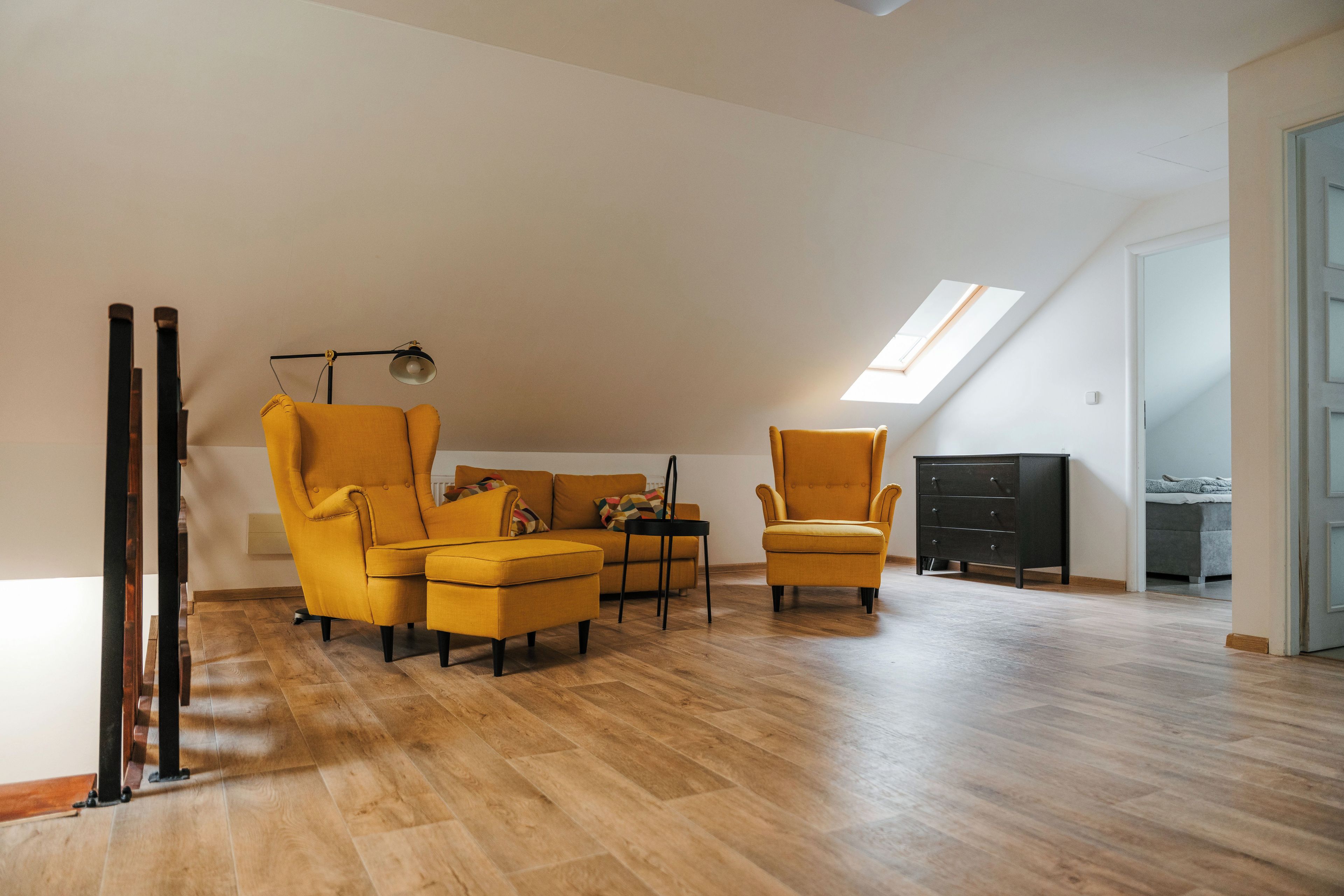 A modern living room with a high ceiling, wooden flooring, and a skylight.