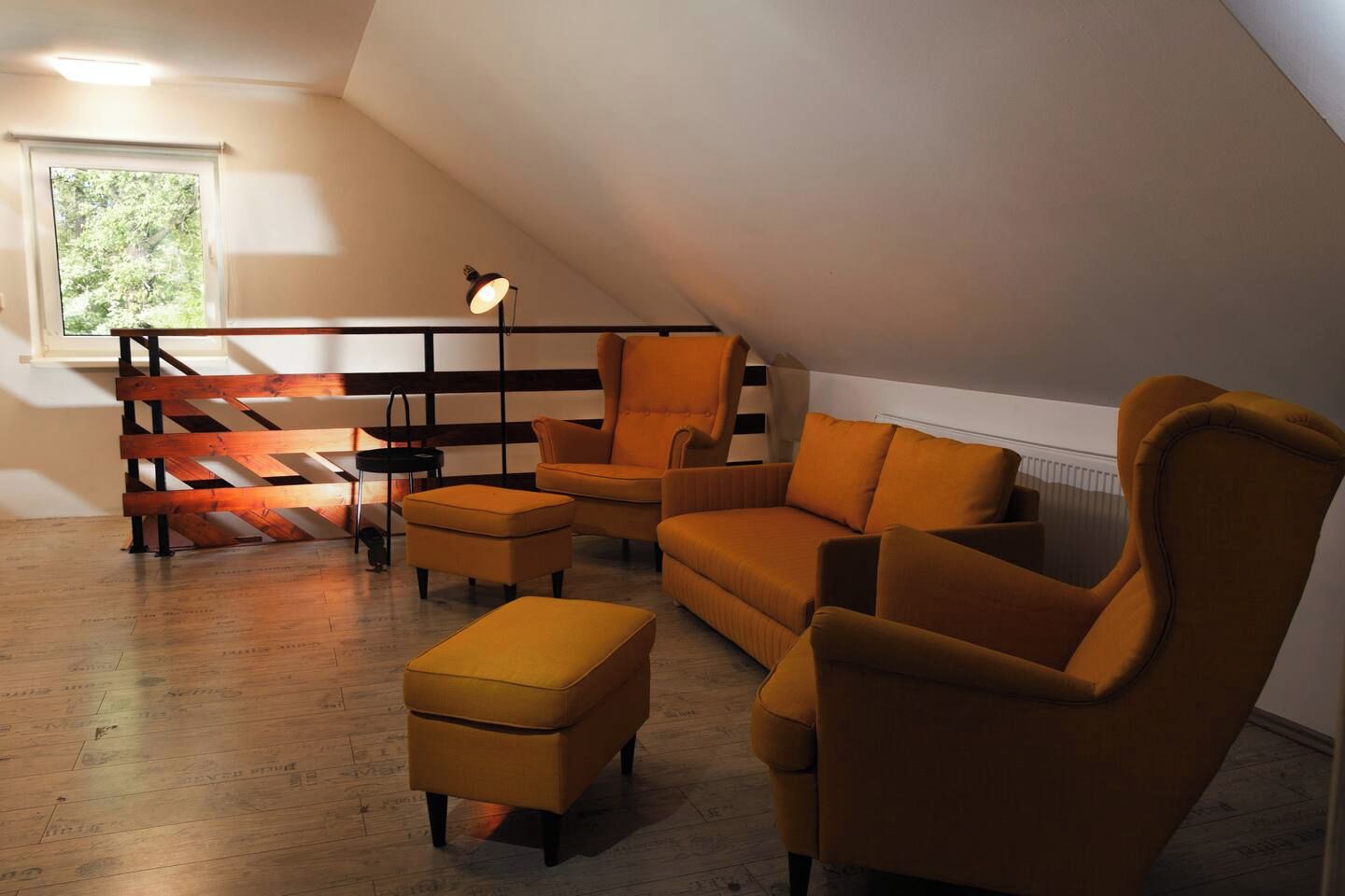A loft-style room with a sloped ceiling, a wooden staircase, and a seating area with a sofa and armchairs.
