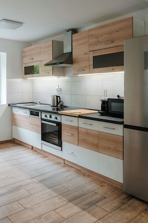 A modern kitchen with wooden cabinets, a stainless steel refrigerator, and a built-in oven.