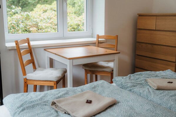 A bedroom with a wooden bed, a small wooden table, two wooden chairs, a window with a view of greenery, and a wooden dresser.
