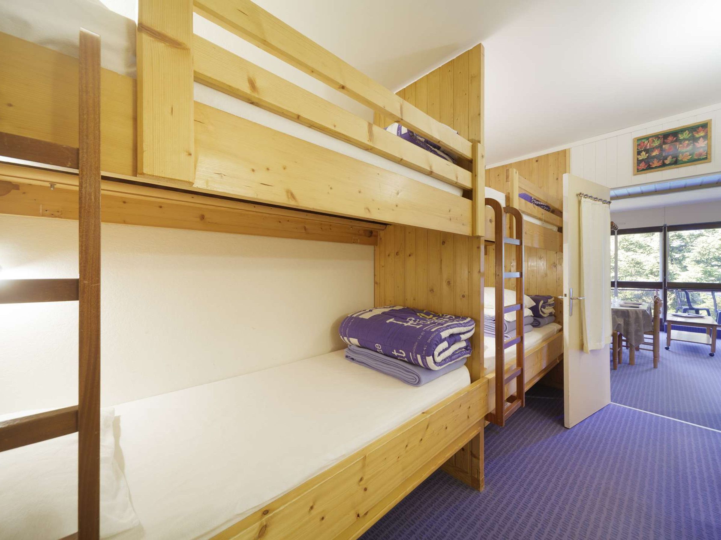 A room with bunk beds, a table, and chairs, with a view of trees through the window.