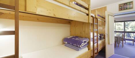 A room with bunk beds, a table, and chairs, with a view of trees through the window.