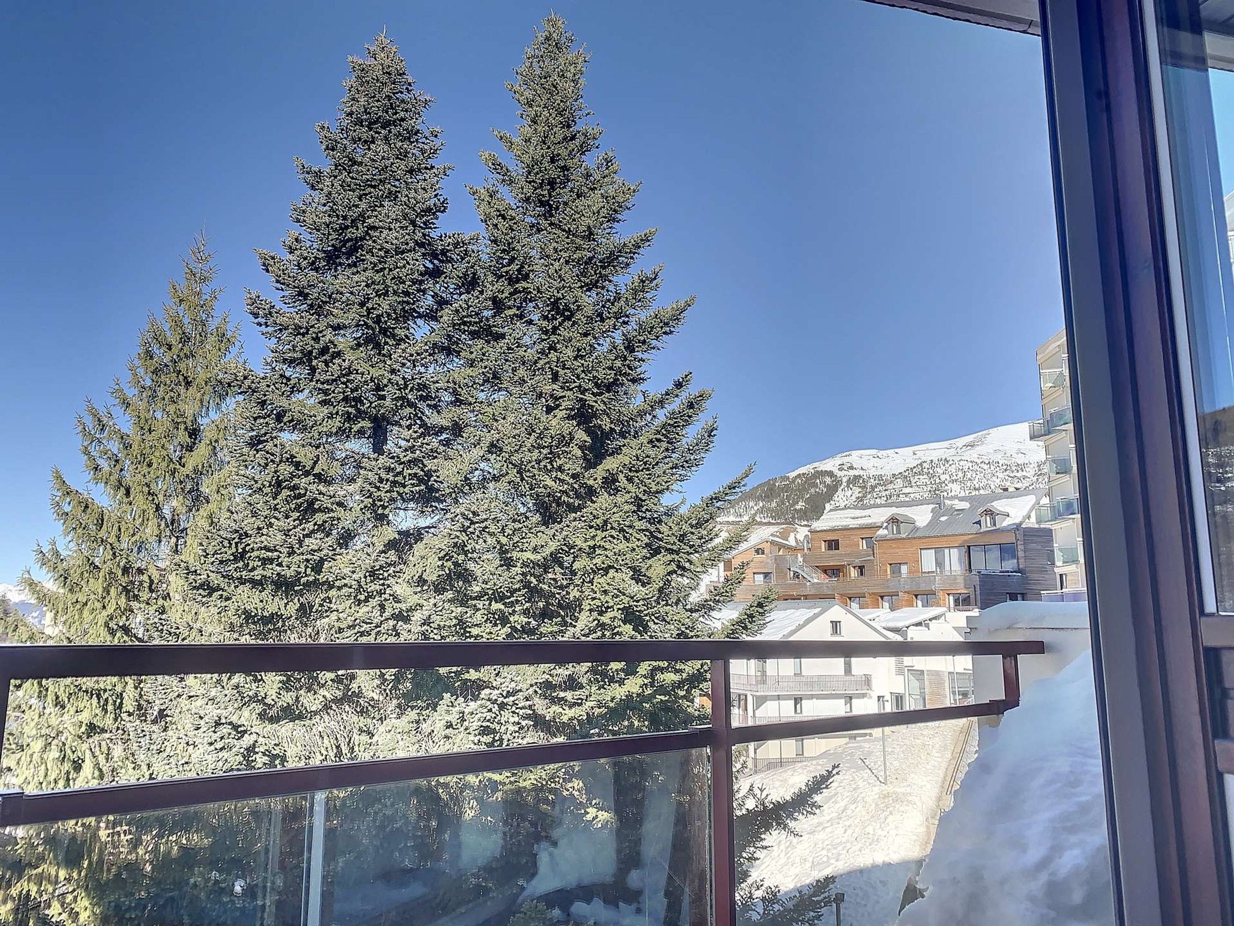 A view of snow-covered trees and a building with multiple balconies.