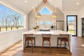 A spacious kitchen with a large island, wooden chairs, and pendant lighting.