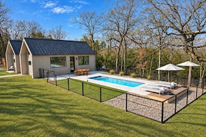 A modern house with a swimming pool, a deck with lounge chairs, and a fenced yard.
