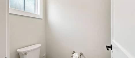 A small, white bathroom with a toilet, a window, and a wall-mounted toilet paper holder.
