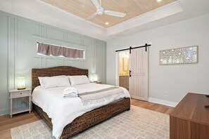 Una camera da letto con un letto, comodini, una ventola a soffitto, una finestra con tende, una porta e un'opera d'arte appesa al muro.