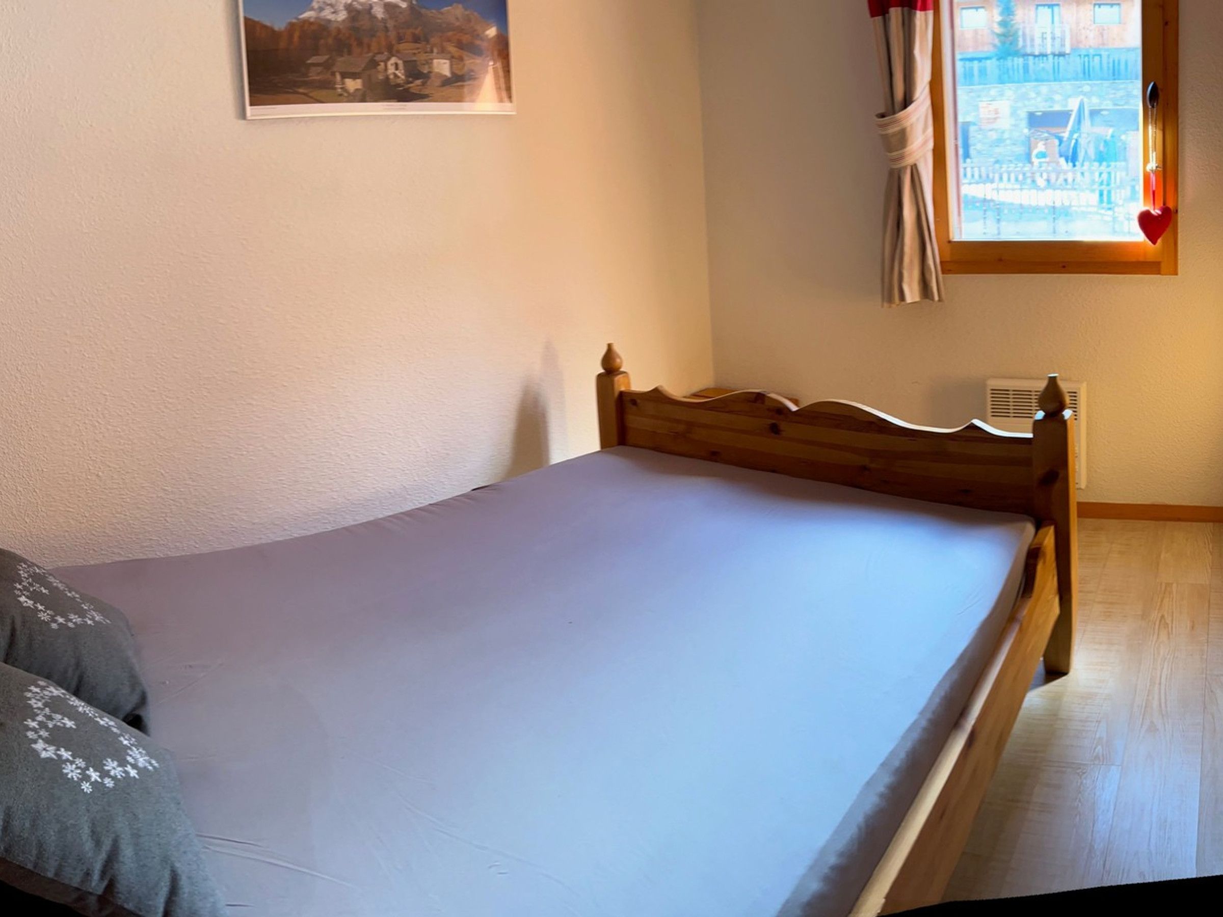 Een eenpersoonsbed met een houten hoofdbord in een kamer met een raam, een wandairconditioner en een lijst met een afbeelding boven het bed.