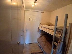 Ein kleines Zimmer mit Etagenbetten, einer weißen Tür und einem kleinen Fenster.