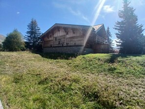 Ein hölzernes Gebäude mit geneigtem Dach, umgeben von Gras und Bäumen.