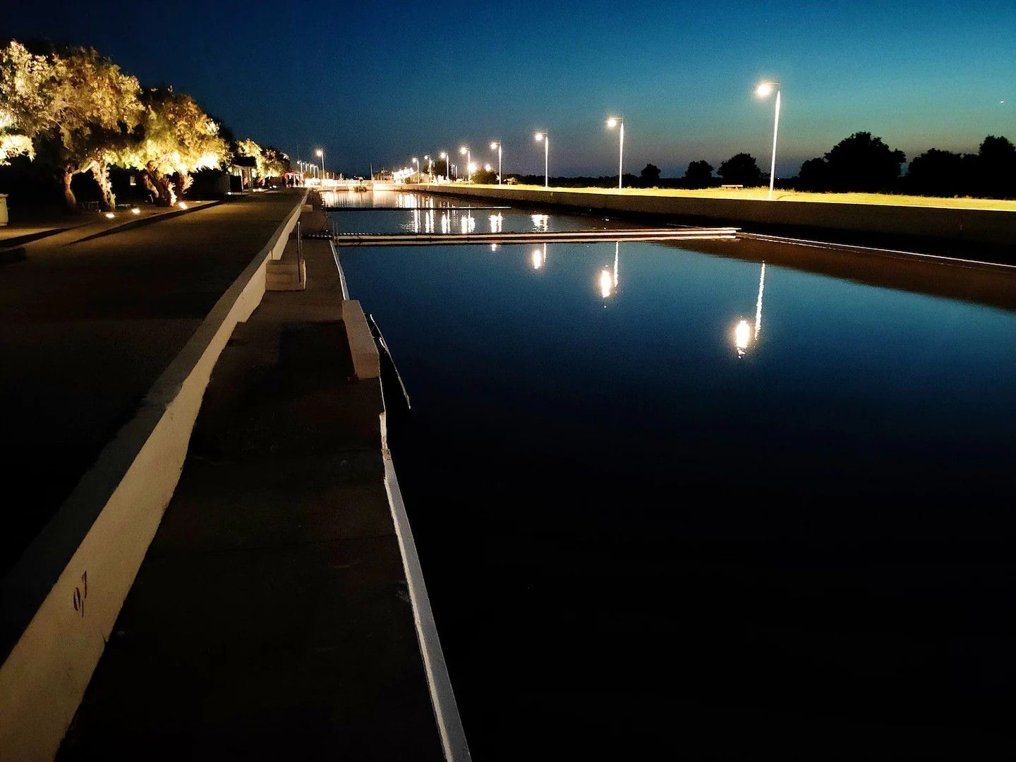 Vista nocturna de una carretera con un cuerpo de agua reflectante y farolas.