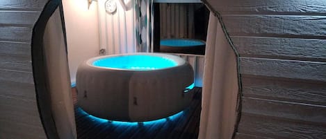 Un jacuzzi circulaire avec un éclairage bleu, installé dans une pièce en bois dont le plafond est incliné.