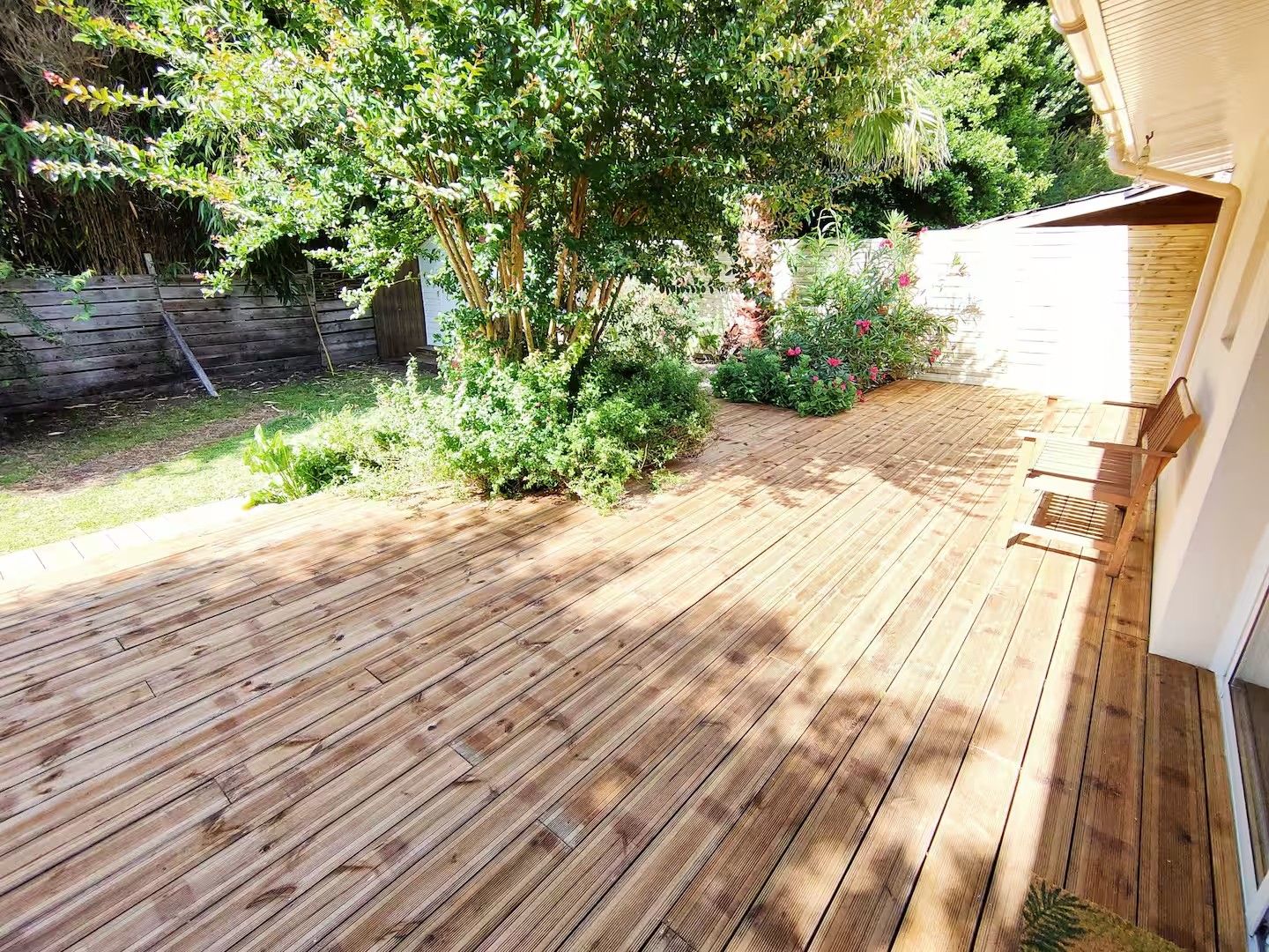 Una terraza de madera con vistas a un jardín y un edificio.