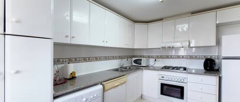 A modern kitchen with white cabinets, a washing machine, a microwave, an oven, and a coffee maker.