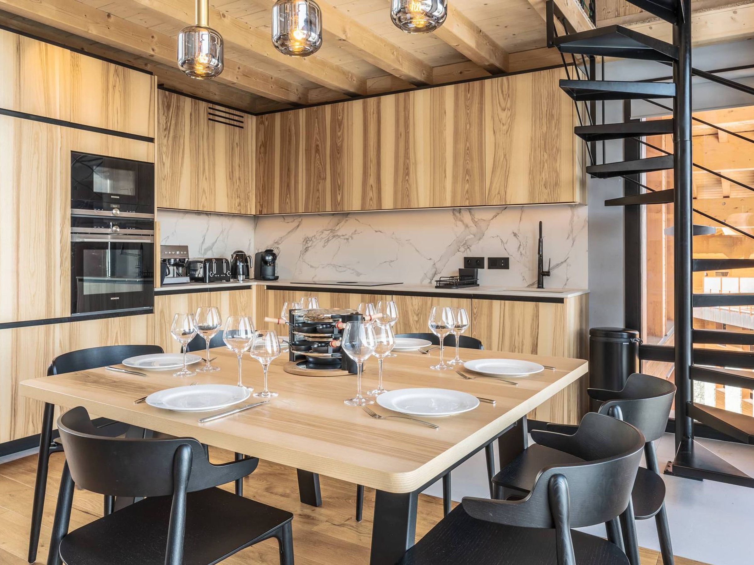 A modern kitchen with wooden cabinetry, a marble backsplash, and a black spiral staircase.