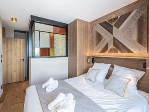 A modern bedroom with a large bed, wooden accents, and a unique geometric wall design. - Duplex apartment with spa - 3 bedrooms - Arc 1800 (Les Arcs 1800)