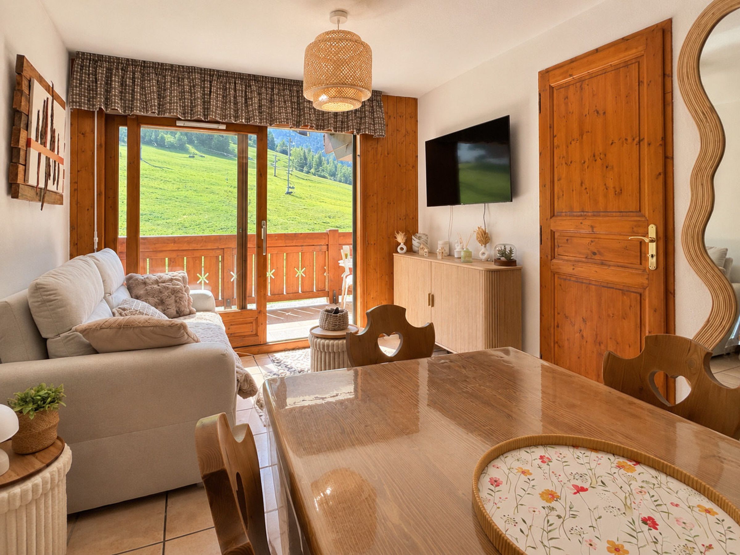 A cozy living room with a sofa, a dining table, and a TV mounted on the wall.