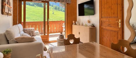 A cozy living room with a sofa, a dining table, and a TV mounted on the wall.