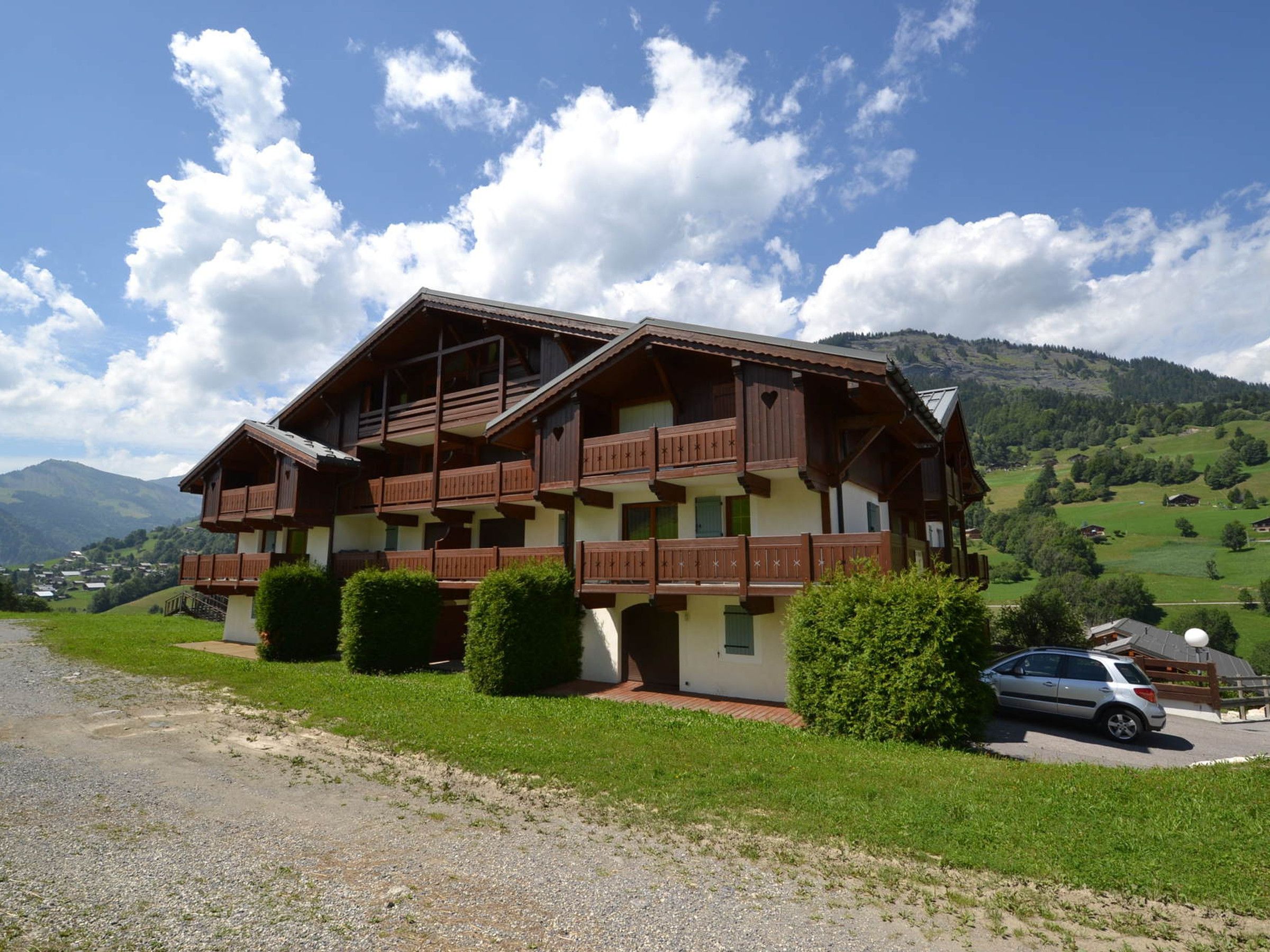 A two-story chalet with wooden balconies, set against a mountainous backdrop.