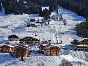 A snow-covered ski resort with chalet-style buildings, ski slopes, and a ski lift. - Apartment with slope view - 6 guests (Flumet)