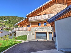 En tvåvånings chalet i trä med en fasad av sten, en balkong och ett garage.