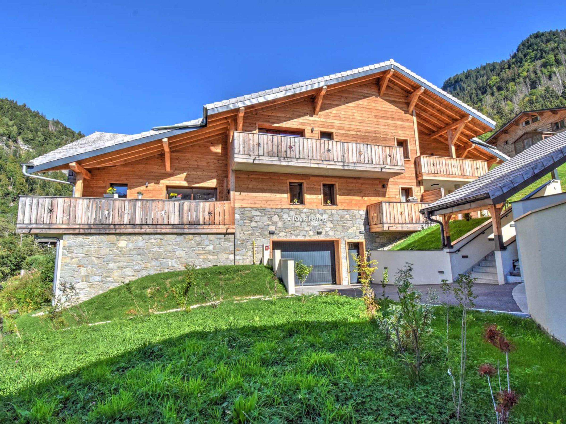 Un chalet in legno a più piani con balconi, basamento in pietra e immerso in un contesto collinare.