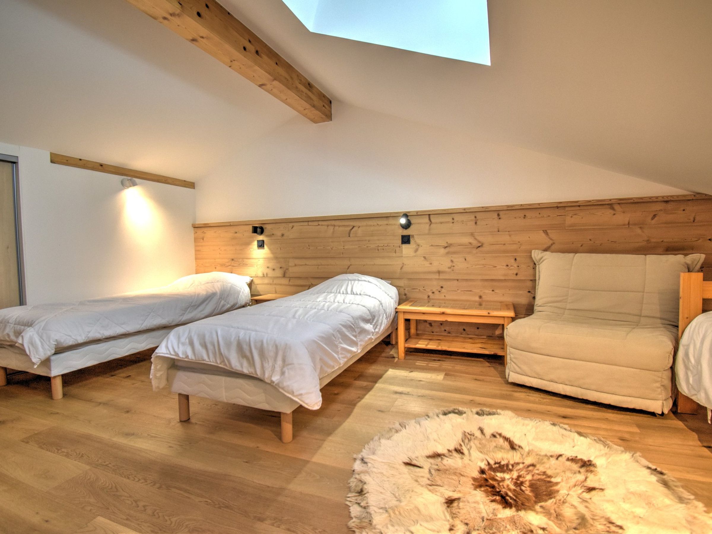 Una habitación con dos camas individuales, un banco de madera, un sofá y una alfombra de piel.