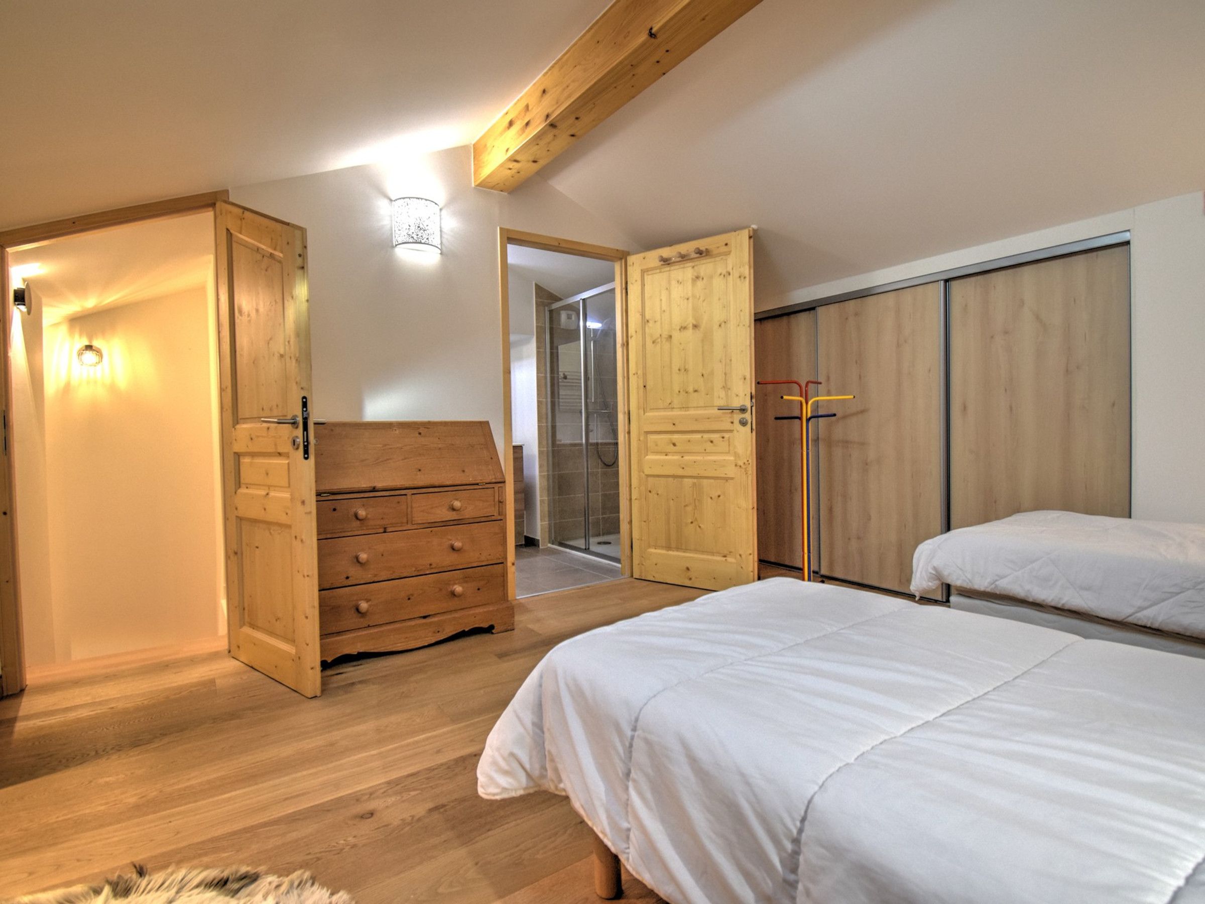 Een slaapkamer met houten vloeren, een houten dressoir, een kast en twee bedden.