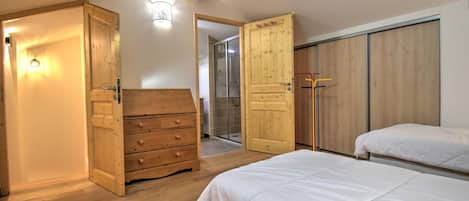 Une chambre avec un plancher en bois, une commode en bois, une armoire et deux lits.