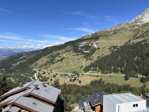 A mountainous landscape with a clear sky, a winding road, and buildings with sloped roofs. - Quiet apartment near slopes - 4 guests (Les Allues)