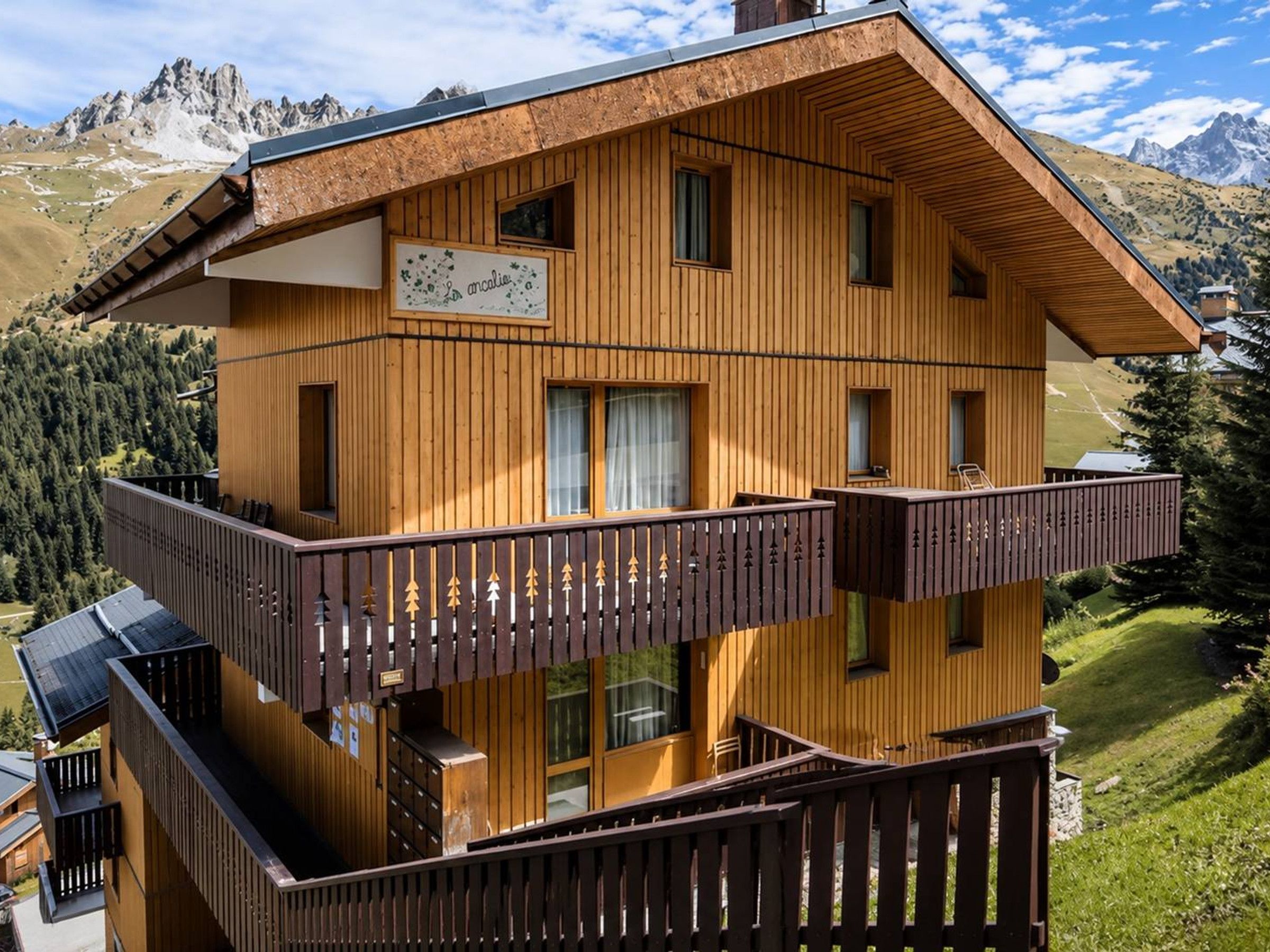 Ein mehrstöckiges Holzchalet mit Balkonen vor einer Bergkulisse.