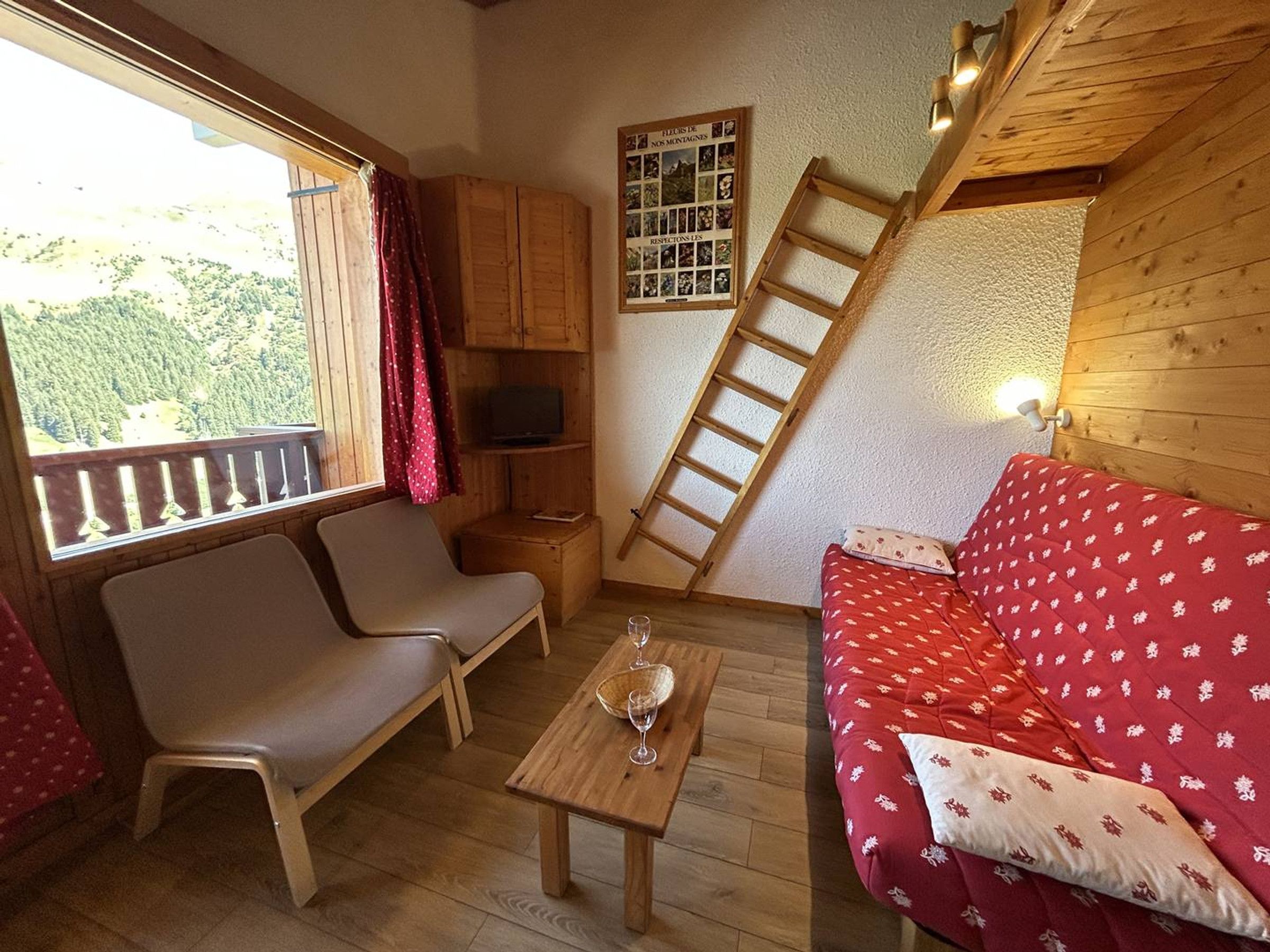 Um quarto aconchegante com piso de madeira, um sofá, uma mesa com um copo, uma TV e uma escada.