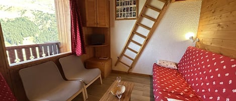 A cozy room with a wooden floor, a sofa, a table with a glass, a TV, and a ladder.