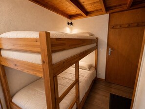 A bunk bed with a wooden frame and white bedding, a wooden door, and a wall-mounted light fixture. - Quiet apartment near slopes - 4 guests (Les Allues)