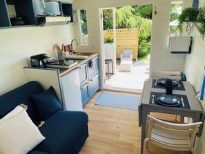 A compact kitchen with a dining area, a sofa, and a view of the garden. - Cozy Travel Trailer in Normandy (Offranville)