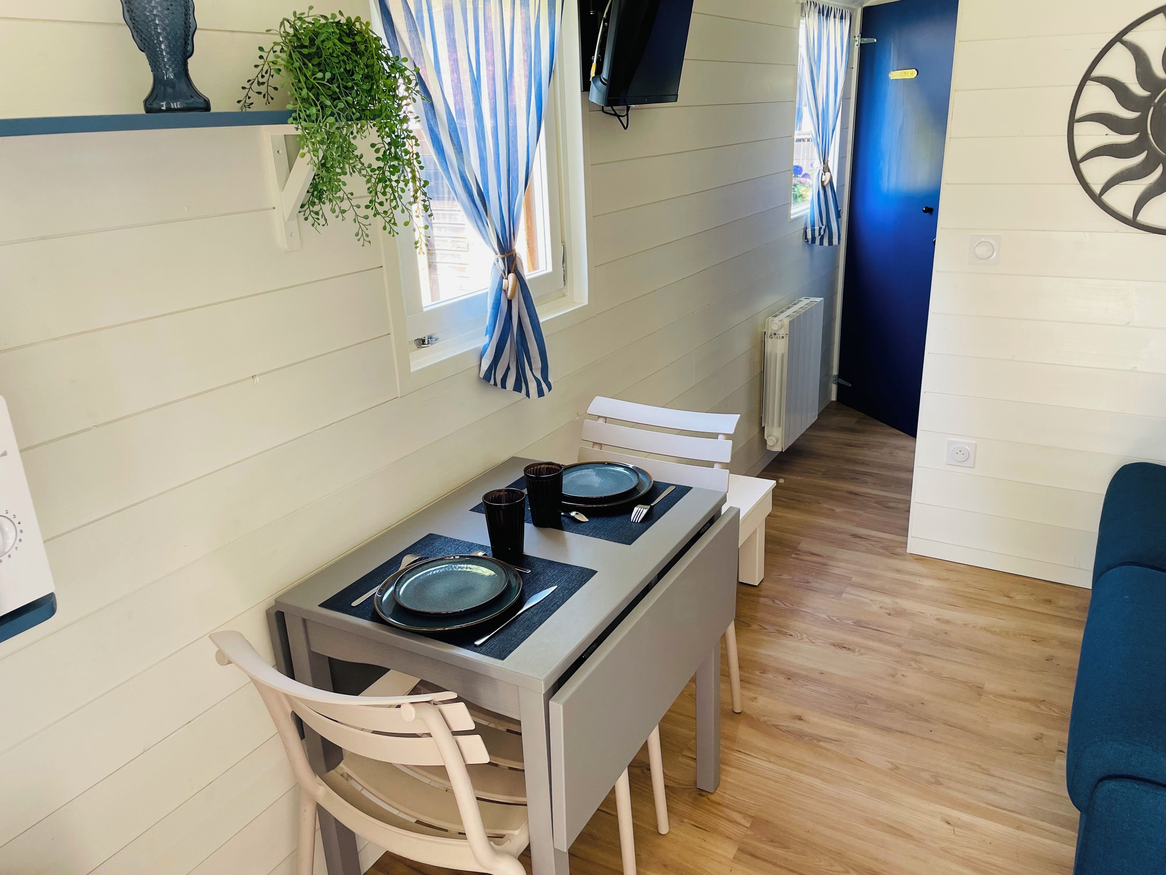 A small dining area with a table set for two, a chair, a potted plant, and a radiator.