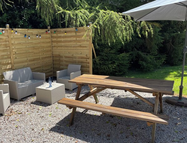 Un patio al aire libre con una mesa de madera y bancos, rodeado por una valla de madera y follaje.