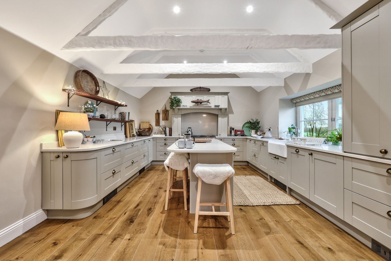 A modern kitchen with a central island, wooden flooring, and white cabinetry.