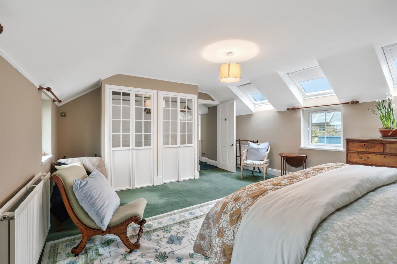 A bedroom with a skylight, a bed, a chair, a dresser, and a window.