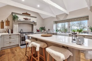 Een moderne keuken met een groot schiereiland, houten krukken en uitzicht op de omgeving.