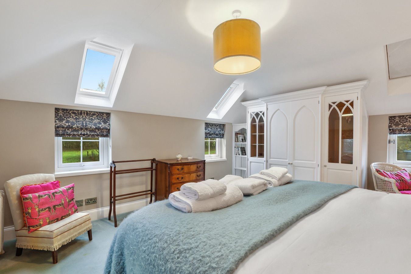 A bedroom with a bed, a chair, a dresser, a wardrobe, and a skylight.