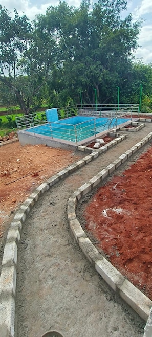 A swimming pool with a metal frame and steps leading into it, surrounded by a concrete border and a dirt path.